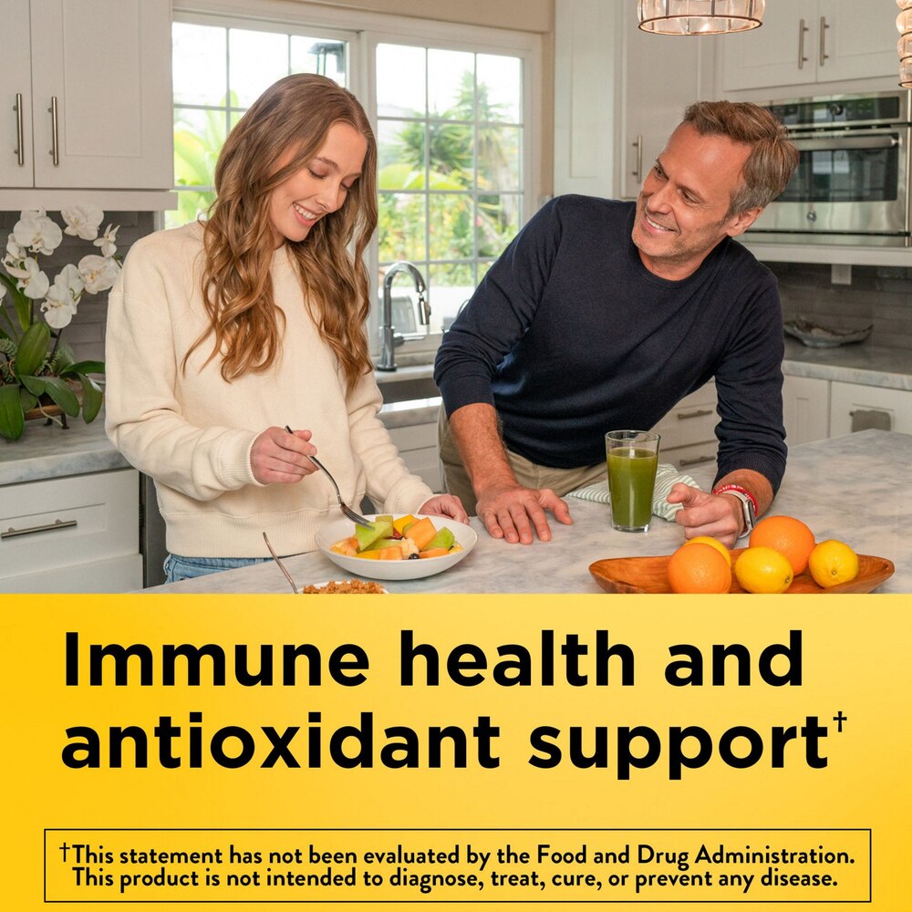 Man and woman in a kitchen with fruits and a glass of juice, promoting immune health and antioxidant support.