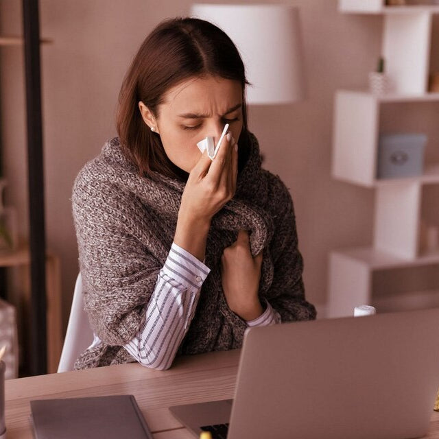 Person at a desk with a laptop, blowing their nose, with text about cold and flu relief.