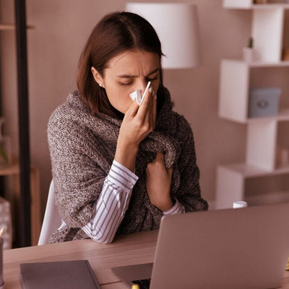 Person at a desk with a laptop, blowing their nose, with text about cold and flu relief.