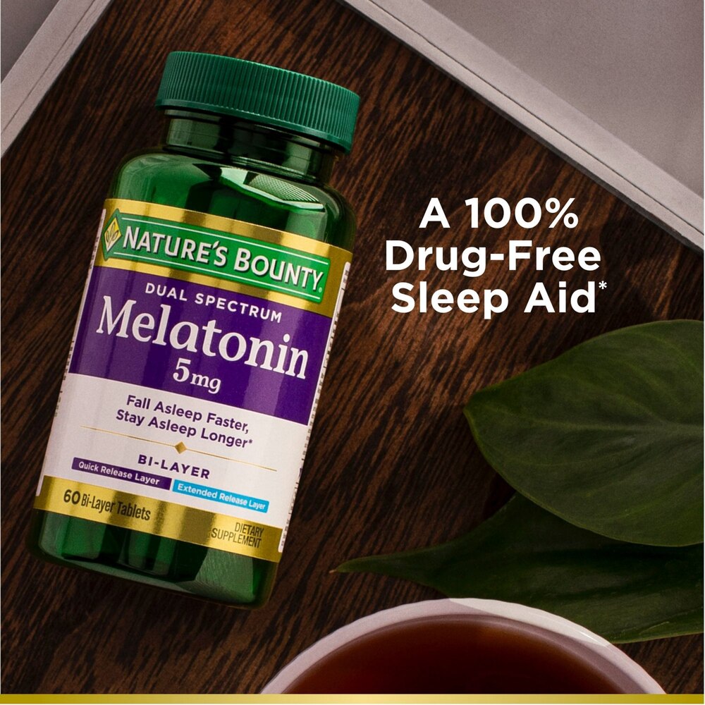 Nature's Bounty Melatonin supplement bottle on a wooden surface with tea and leaves.